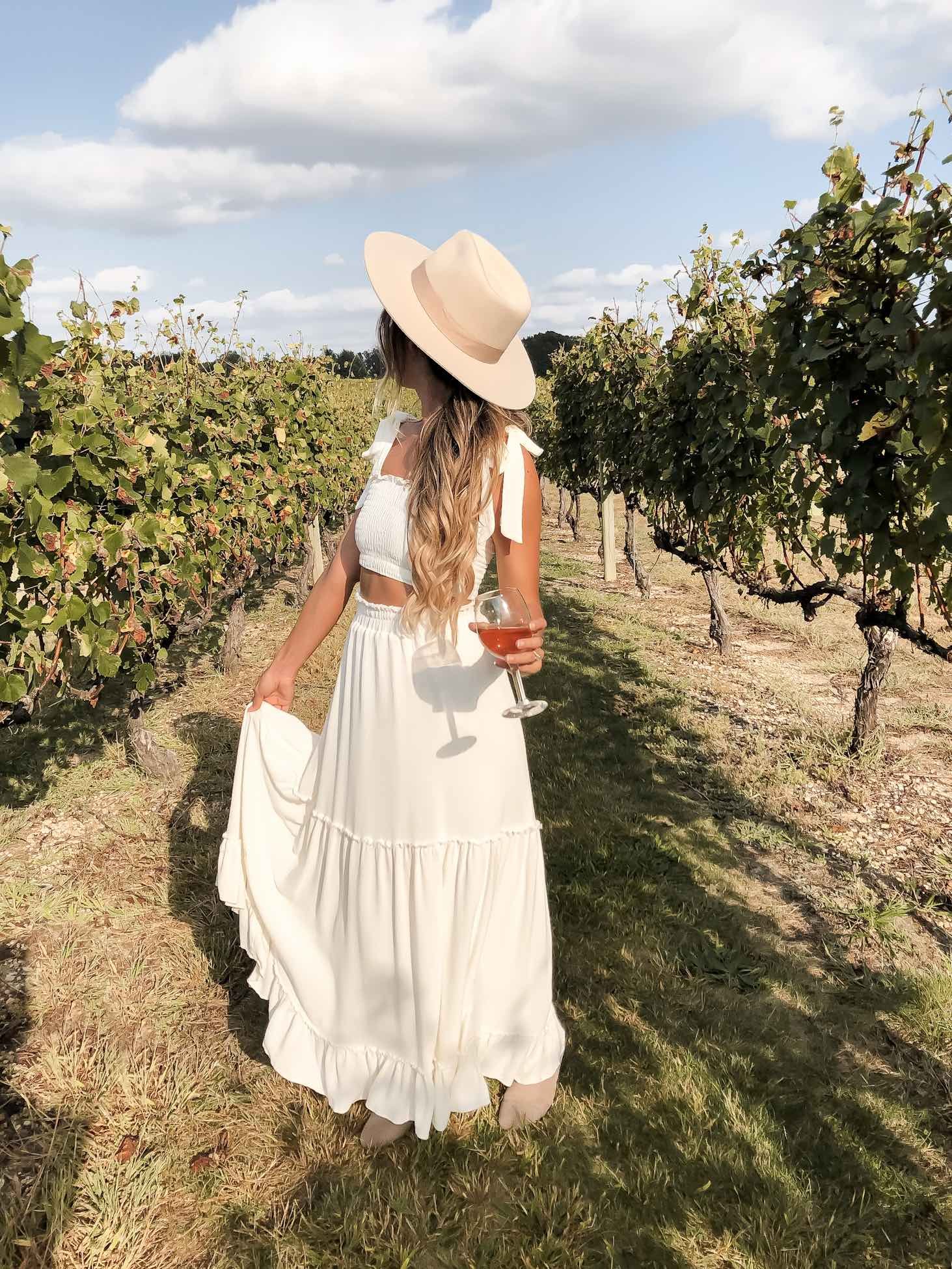 Woman in a stylish outfit walking through vineyard rows at a winery